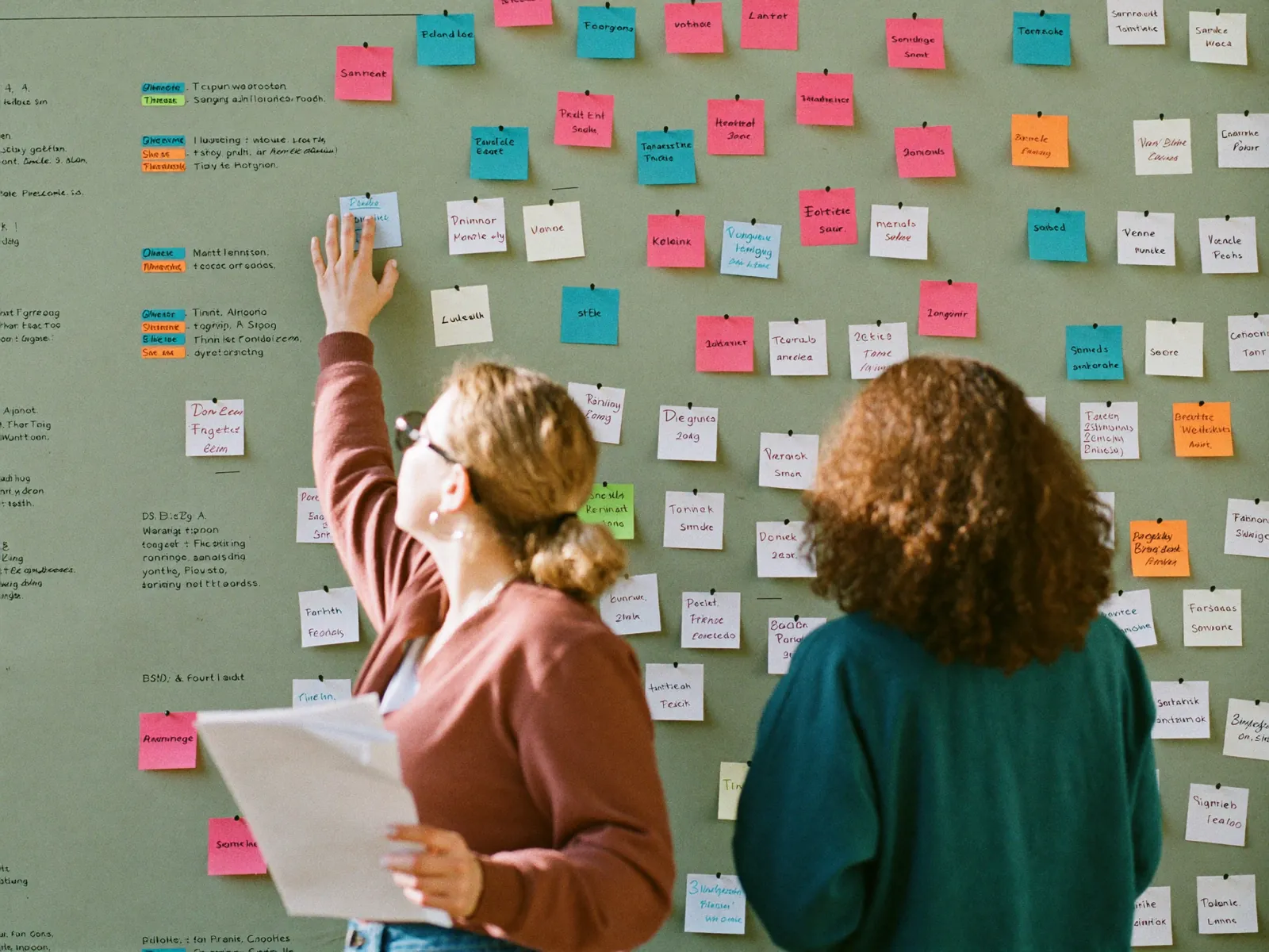 Two researchers grouping colour-coded sticky notes into themes on a wall